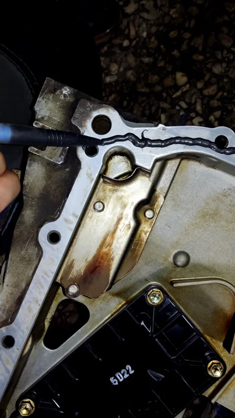 A nozzle squeezes grey liquid sealant onto a clean metal car oil pan edge Stock Footage 336559824