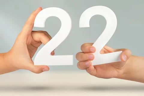 Number two two in hand. Hand holding white number 22 on blurred background with Stock Photos