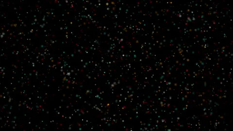Numerous small, colored particles gently float across a dark, blurred Stock Footage 344240672