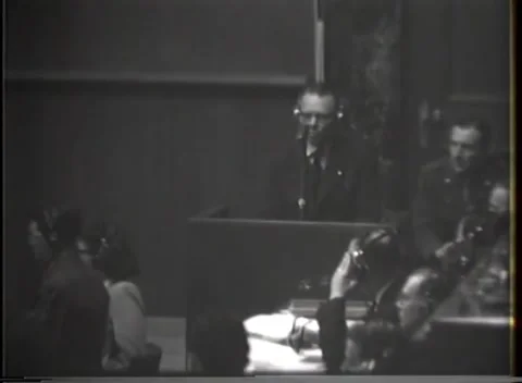NUREMBERG - 1946: War crimes hearing — Seated group beside shadowed witness Vidéo 343320823