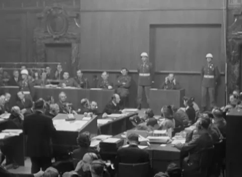 NUREMBERG, GERMANY - 1946: Bench huddle - Standing lawyer faces occupied dock Stock Footage 344490342