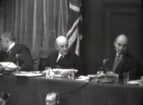 NUREMBERG, GERMANY - 1946: Folded flag - Suited members sit at bench Stock Footage 344901666