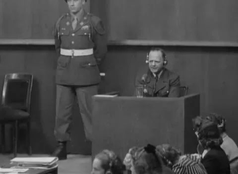 NUREMBERG, GERMANY - 1946: Square portrait - Guard stands beside focused witness Stock Footage 344490282