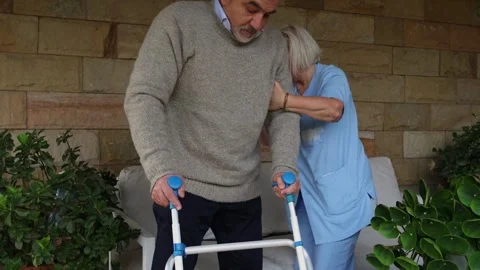 Nurse assisting elderly man using walker to sit down Stock Footage 300171821