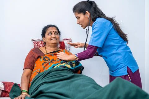 Nurse checking health of middle aged woman at nursing home using stethoscope - Stock Photos