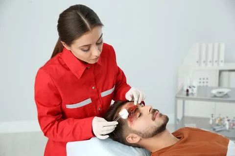 Nurse cleaning young man's head injury in clinic. First aid Stock Photos