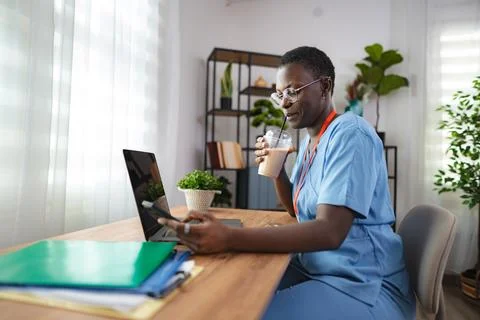 Nurse drinking coffee and using smartphone during break at home office Stock Photos