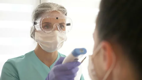 Nurse in a medical mask and glasses measures the patient's temperature with a Stock Footage