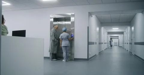 Nurse with old patient wait for elevator in medical center hallway Stock Photos