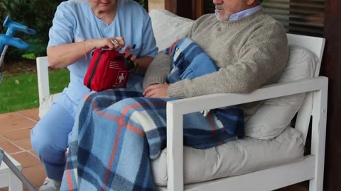 Nurse opening first aid kit assisting elderly man sitting on couch Stock Footage 300171926