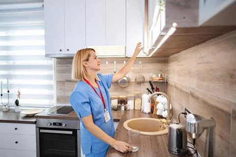 Nurse opening kitchen cabinet while holding glass of water Stock Photos
