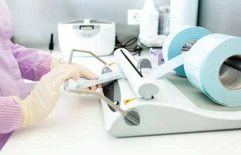 Nurse packing dental instruments using sealing machine in clinic Stock Photos