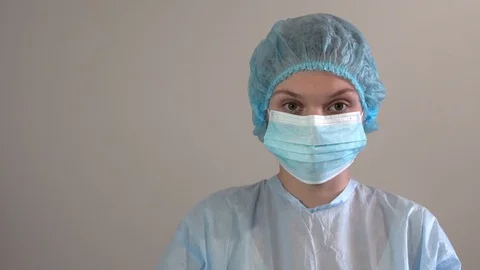 A nurse in a protective mask is looking into the camera. in sterile uniform. Video stock 127849737