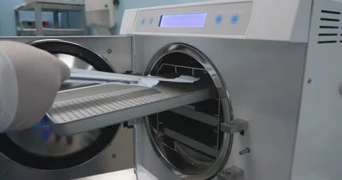 The nurse pulls out a shelf in the autoclave and puts the wrapped surgical Stock Footage 221567071