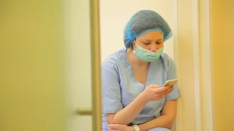 The nurse is resting between operations. writes SMS. sterile mask on her face Stock Footage 125470901