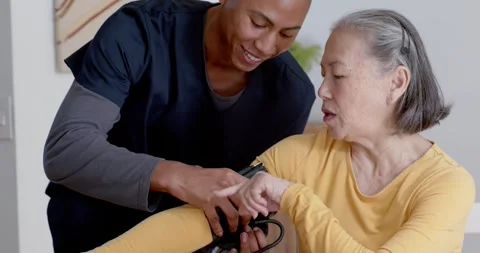 Nurse in scrubs fitting cuff for BP check, Senior Chinese woman extending arm at Stock Footage 345541732