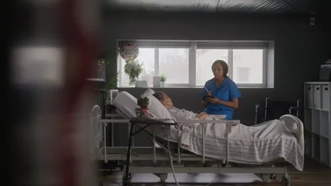 Nurse in Scrubs Takes Notes While Helping Elderly Patient in Hospital Room Stock Footage 208798531