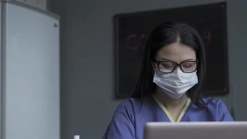 A nurse sits on a shift at a computer and enters data into patient profiles. The Stock Footage 130174984
