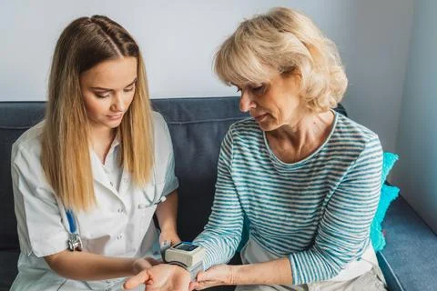 Nurse sitting down on the couch with elderly lady, while taking her blood Stock Photos