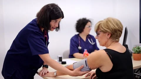 Nurse talking to a patient while measuring blood pressure Vídeos de archivo 261097550