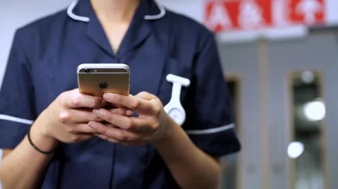 Nurse using cellular mobile phone in front of doors in hospital 스톡 동영상 59087328