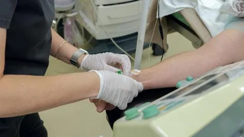 Nurse wearing protective gloves inserts intravenous cannula into patient forearm Stock Photos
