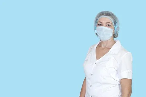 Nurse in white coat, cap and mask on blue isolated background. European woman Фото