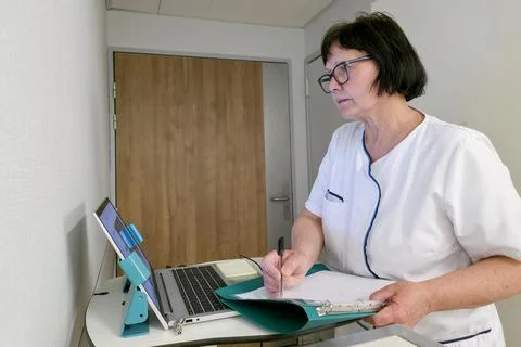 Nurse works on a computer while writing notes Stock Photos