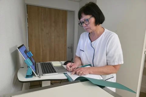 A nurse is writing notes while using a computer Stock Photos