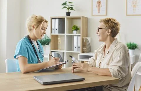 Nurse writing patient notes while consulting senior woman in clinic office Foto stock