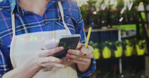 Nursery worker tapping phone, holding pencil, notepad, updating stock, causing Stock Footage 321390166