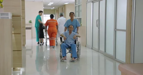 Nurses and paramedics assist elderly asian male patient in wheelchair through Video stock 313999447