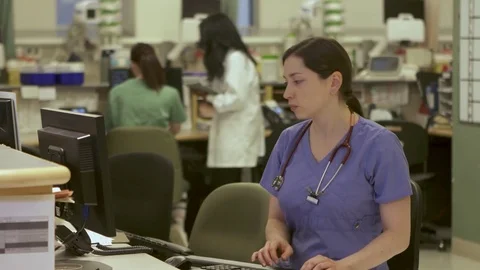 Nurses answers phone in busy nurse's station in a modern hospital. Stock Footage
