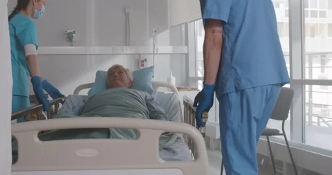 Nurses in protective gloves and mask transport senior patient in hospital Stock Footage 154143100