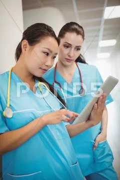 Nurses Using Digital Tablet In Hospital Corridor