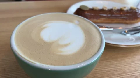 Nut and chocolate eclair and glass of flat white coffee on black plate Stock Footage 264717773