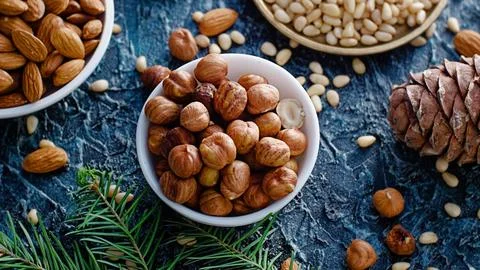 Nut assortment. Hazelnuts, almonds, pine nuts in plates stand on table with Stock Photos
