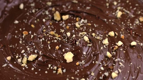 Nut pieces falling down into brown melted milk chocolate spread close up Stock Footage 274441237