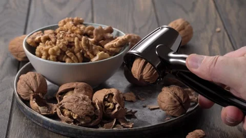 Nutcracker in hand over plate of walnuts on table Stock Footage 305566499