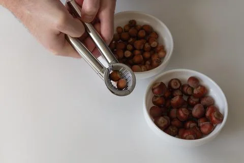 Nutcracker in men's hands, different varieties of hazelnuts in plates Foto stock