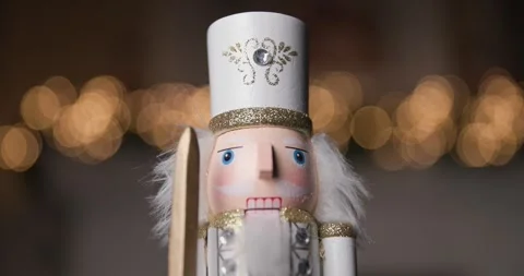 Nutcracker in a white costume, holding a sword, illuminated by golden bokeh Stock Footage 287176856