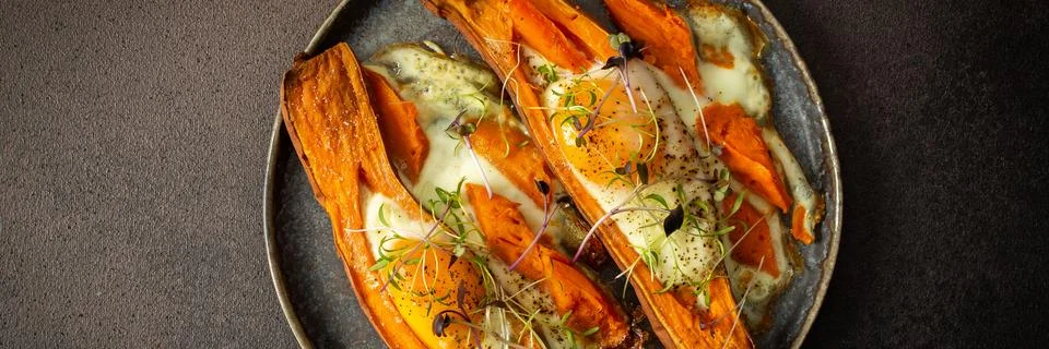 Nutrient-rich eggs baked inside sweet potatoes sit on a rustic plate. Fresh.. Stock Photos