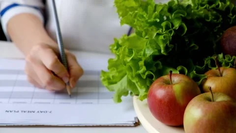 Nutritionist woman writing diet plan on table full of fruits and vegetables Stock Footage