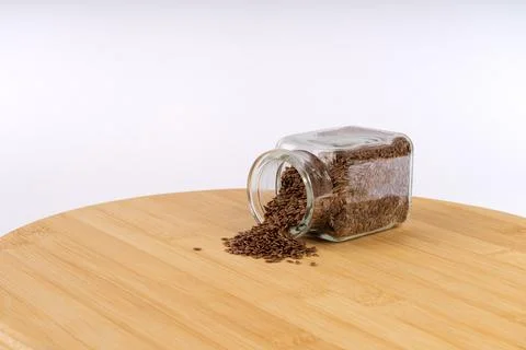 Nutritious Flax Seeds Gently Spilling from a Clear Glass Jar onto a Warm Wo.. Stock Photos