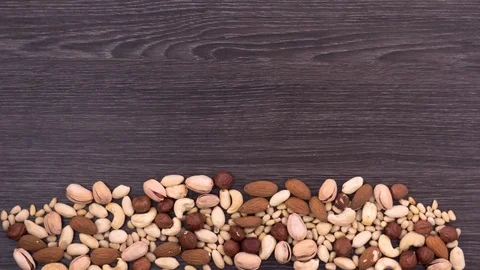 Nuts fall and form a word vegan on the dark wooden background. Stop motion Stock Footage 72683947