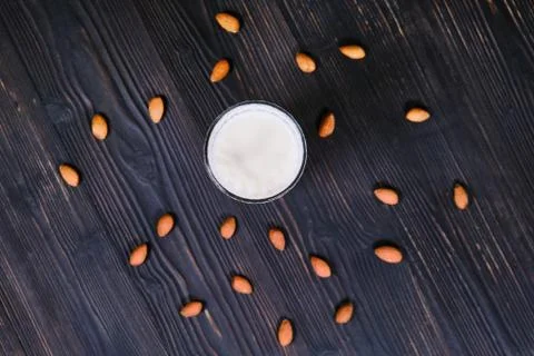 Nuts scattered on a table, top view. Almond milk on a black wood background.  Stock Photos