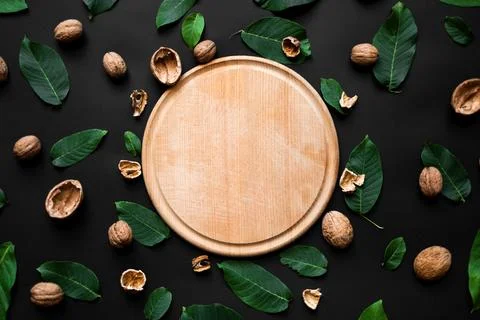 Nutshell and fresh green leafs scattered on a black background. Wooden cutt.. Stock Photos