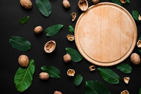 Nutshell and fresh green leafs scattered on a black background. Wooden cutt.. Stock Photos