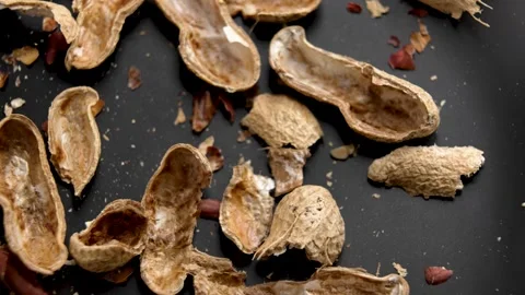 Nutshells of eaten peanuts falling on black surface Video stock 309609977