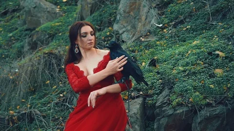 Nymph with raven on hand. Woman in red dress with deep necklinen stroking bird Stock Footage 121885853